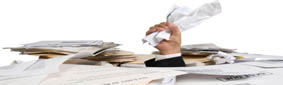 An unorganized pile of paperwork and files, with the hand of a businessman clutching paper sticking out of the clutter.